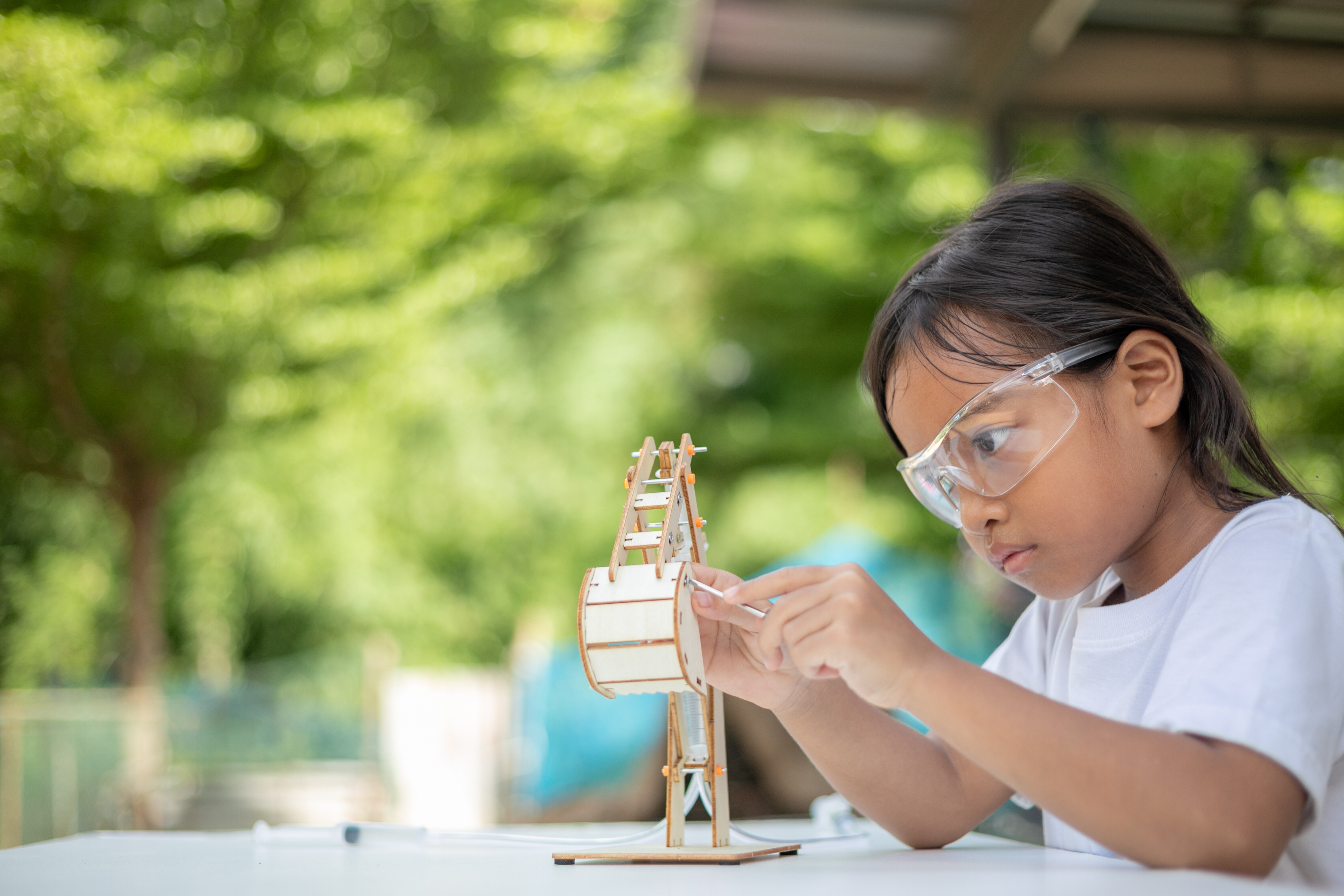 Jonge uitvinder: een meisje met een beschermbril dat een prototype maakt. Op de achtergrond groene natuur.
